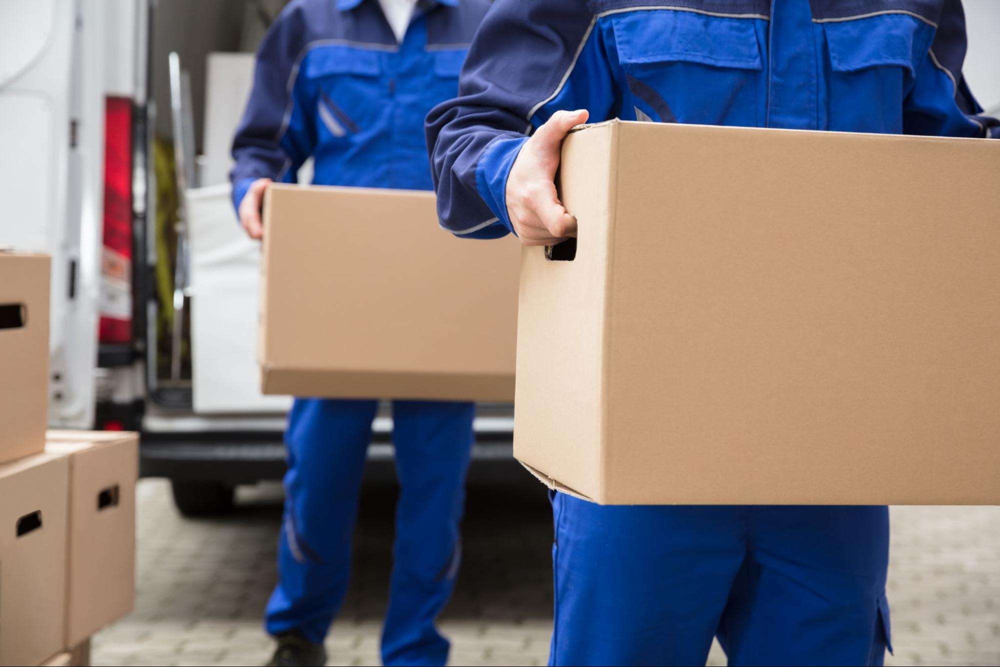 Close-up Of Two Movers Carrying Cardboard Box.