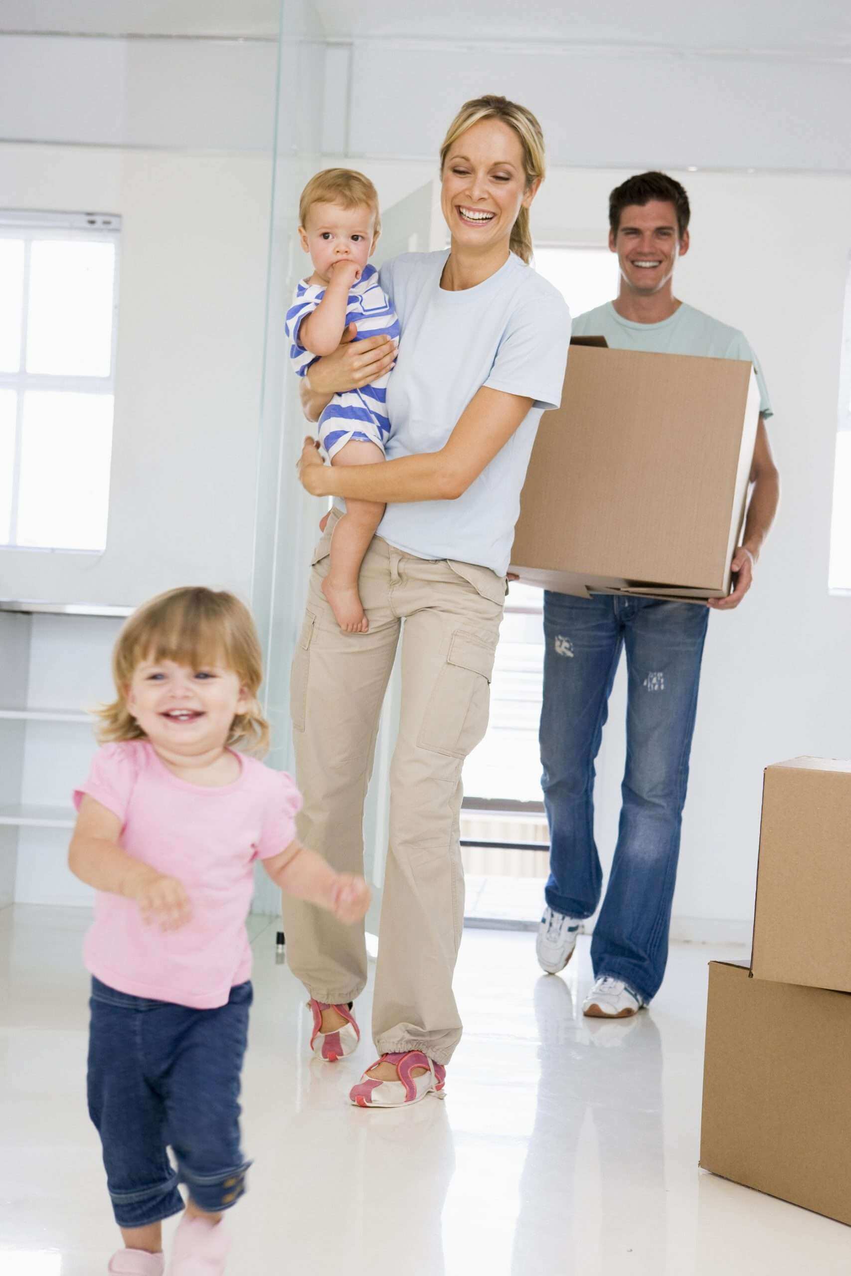 Young family with two small kids walking through white-floored new house with moving boxes, using local mover Las Vegas team