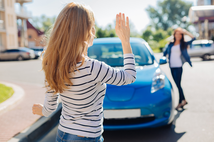Two young women waving at each other in apartment parking lot being good neighbors