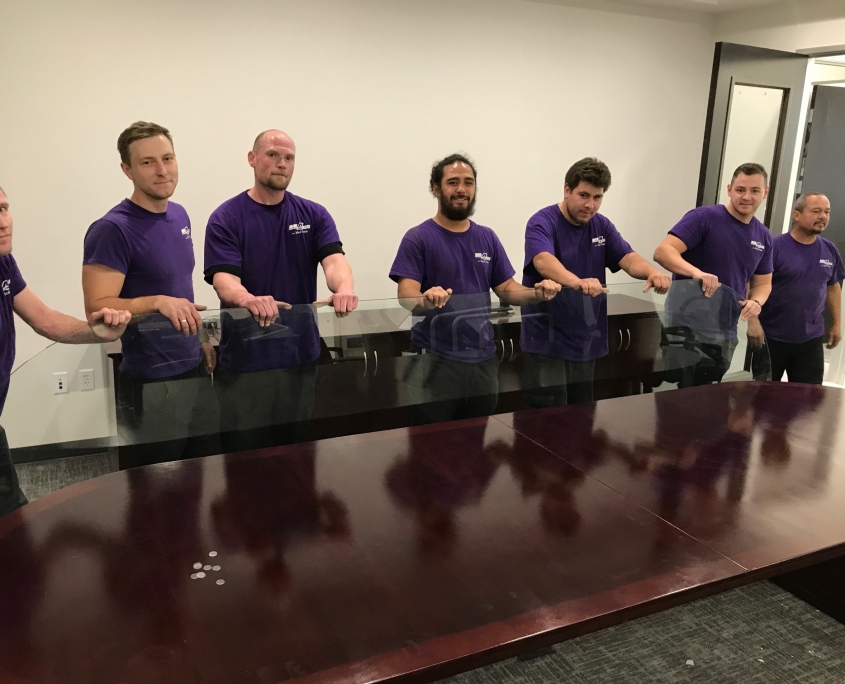 A team of Move 4 Less movers moving heavy glass table into a conference room during a business move
